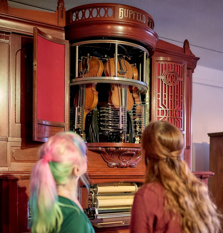 Zwei Besucherinnen stehen vor einem Orchestrion mit sichtbaren Mechanik-Elementen.